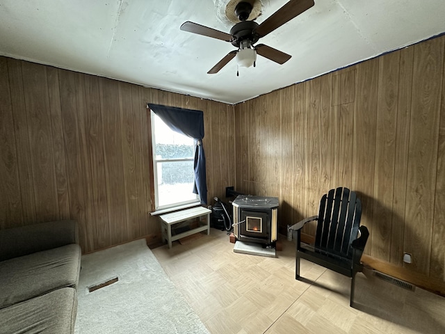 sitting room with a wood stove, ceiling fan, and wood walls