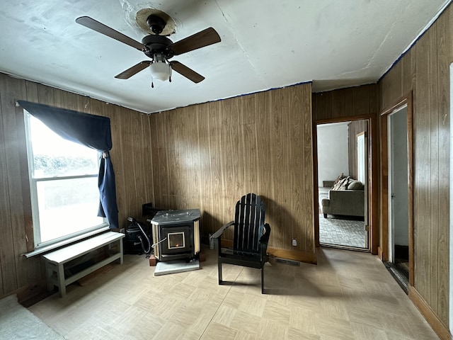 sitting room with light parquet flooring, a wood stove, ceiling fan, and wood walls