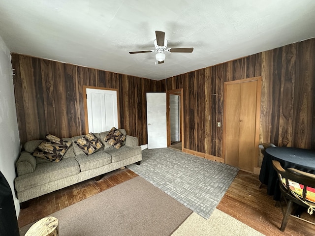 living room featuring ceiling fan, wood-type flooring, and wooden walls