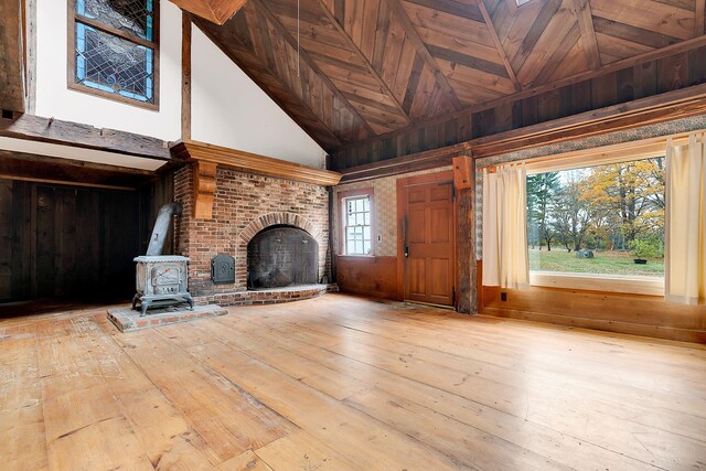 unfurnished living room featuring high vaulted ceiling, wooden walls, light hardwood / wood-style flooring, a fireplace, and wood ceiling