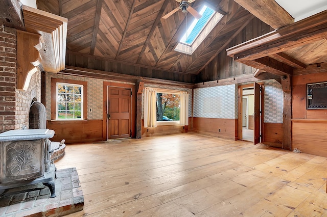 unfurnished living room featuring a wood stove, high vaulted ceiling, wooden walls, light hardwood / wood-style flooring, and ceiling fan