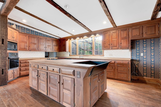 kitchen with vaulted ceiling with beams, a center island, black appliances, and hardwood / wood-style flooring