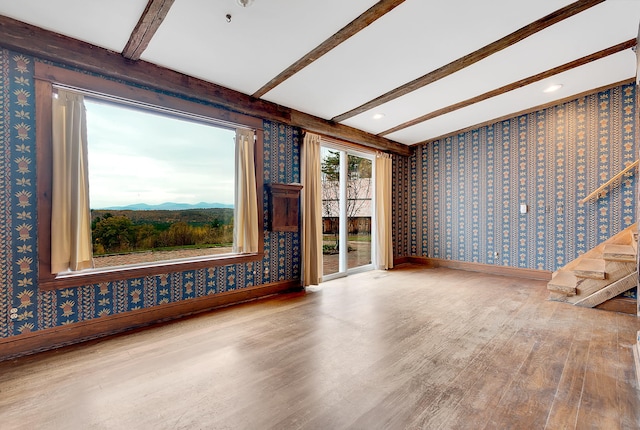 unfurnished living room featuring a mountain view, beam ceiling, and hardwood / wood-style flooring