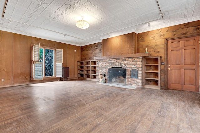 unfurnished living room with a fireplace, wood-type flooring, track lighting, and wood walls