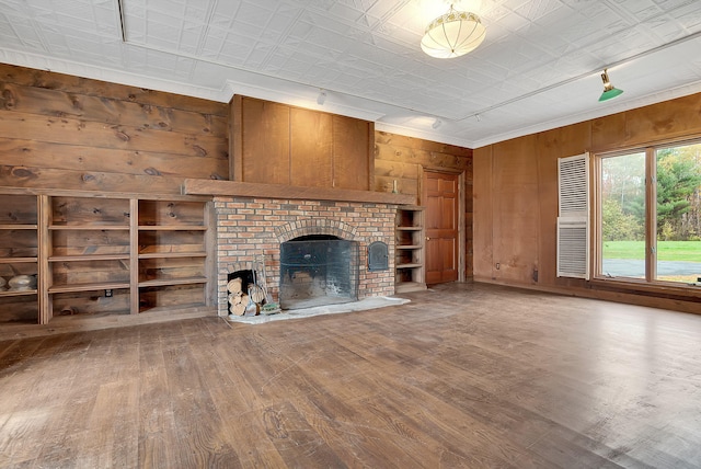 unfurnished living room featuring built in shelves, wood walls, hardwood / wood-style flooring, and a brick fireplace