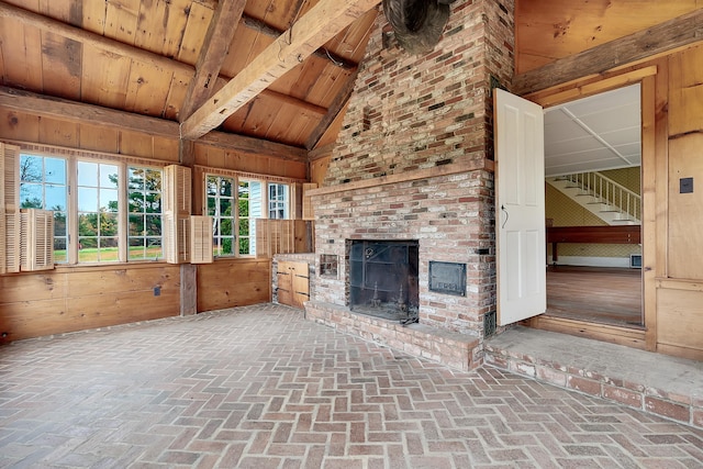 unfurnished living room featuring vaulted ceiling with beams, wooden walls, a fireplace, and wooden ceiling