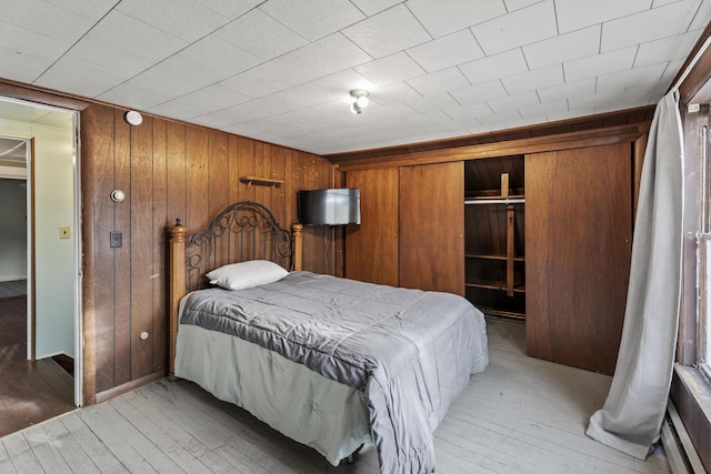 bedroom with light hardwood / wood-style flooring, wooden walls, and a closet