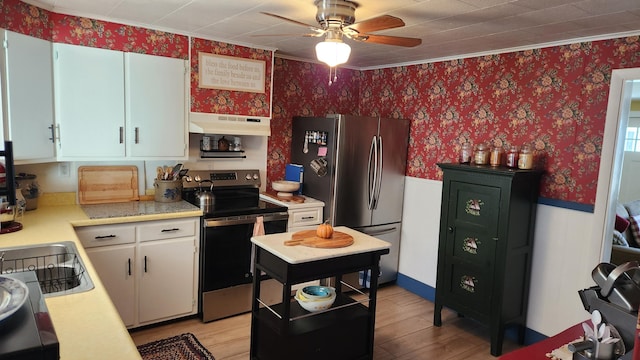 kitchen with under cabinet range hood, stainless steel appliances, white cabinets, light countertops, and wallpapered walls