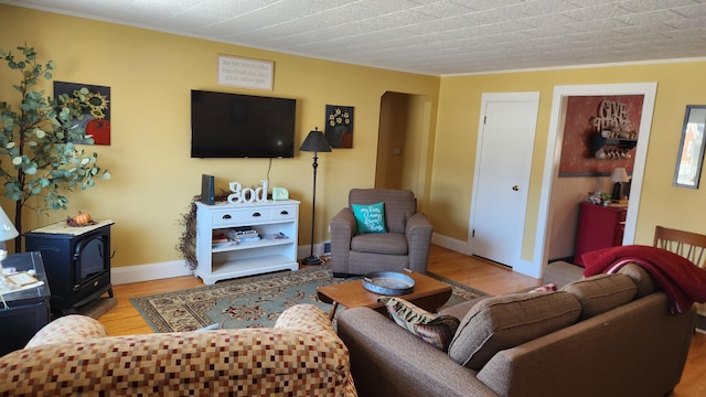 living room featuring a wood stove, baseboards, crown molding, and light wood finished floors