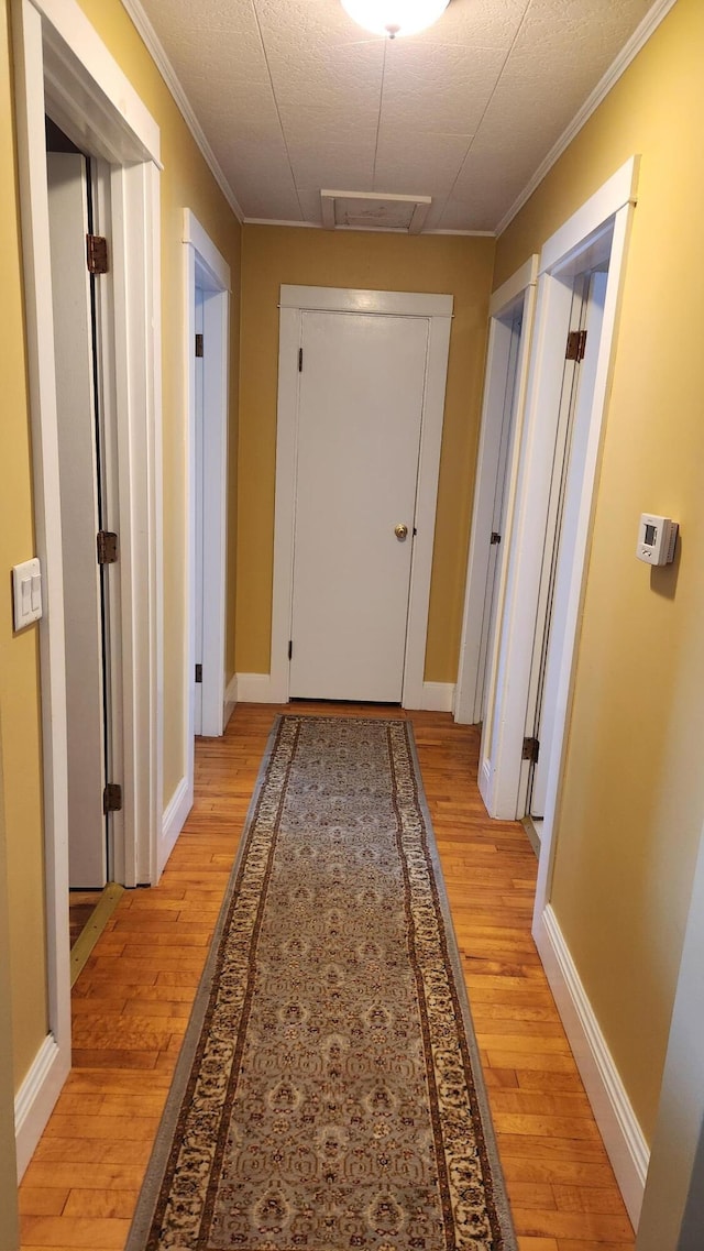 hallway featuring visible vents, baseboards, light wood-style flooring, and crown molding