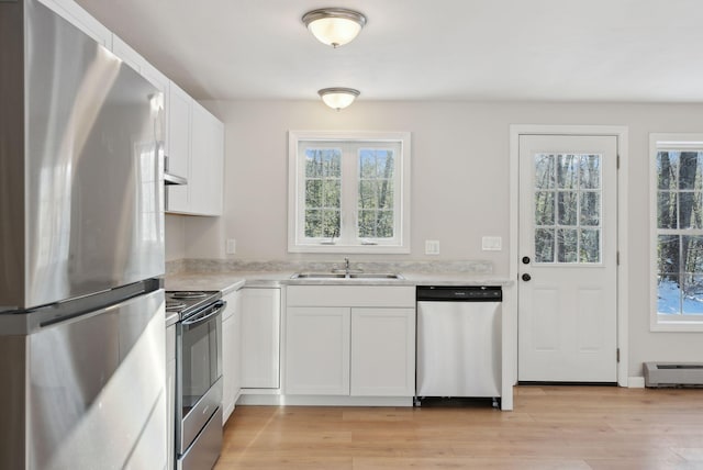 kitchen featuring stainless steel appliances, light hardwood / wood-style floors, a baseboard heating unit, white cabinetry, and sink