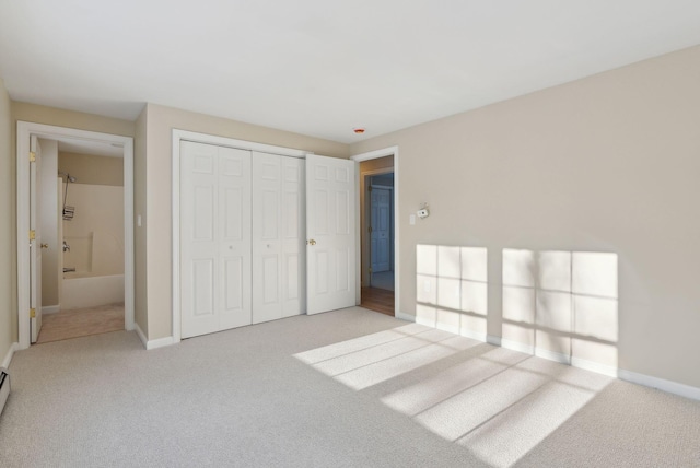 unfurnished bedroom with ensuite bath, light colored carpet, a closet, and baseboard heating