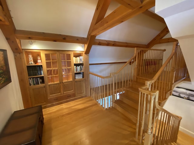 staircase with built in shelves, lofted ceiling with beams, and hardwood / wood-style flooring