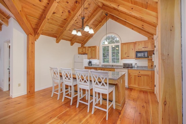 kitchen with a center island, white appliances, decorative light fixtures, light hardwood / wood-style floors, and light stone counters