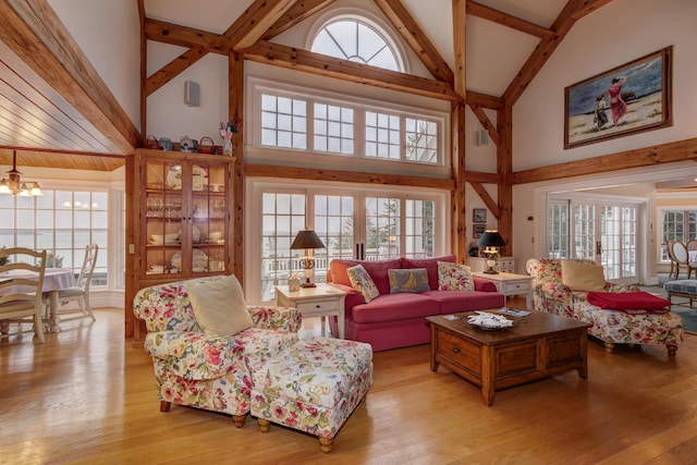 living room with a wealth of natural light, light hardwood / wood-style flooring, a towering ceiling, and a notable chandelier