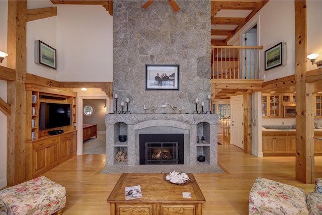 living room with a fireplace, a high ceiling, light hardwood / wood-style floors, and beam ceiling