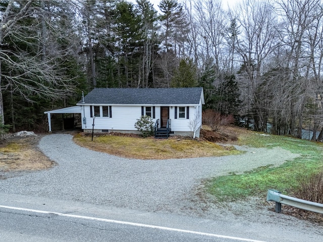 view of front of home featuring a wooded view, crawl space, an attached carport, gravel driveway, and a shingled roof