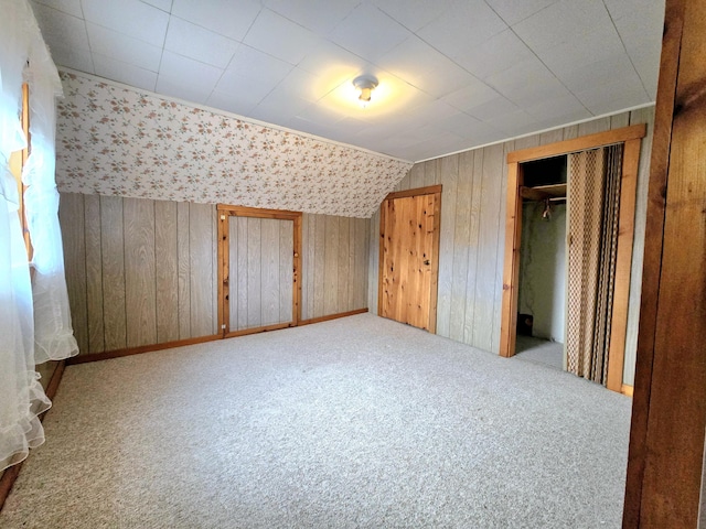 unfurnished bedroom with lofted ceiling, carpet floors, wooden walls, and a closet