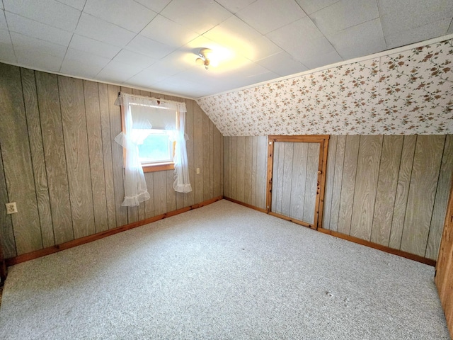 additional living space with light carpet, vaulted ceiling, and wooden walls