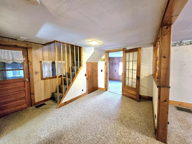 basement with french doors, light colored carpet, and a textured ceiling