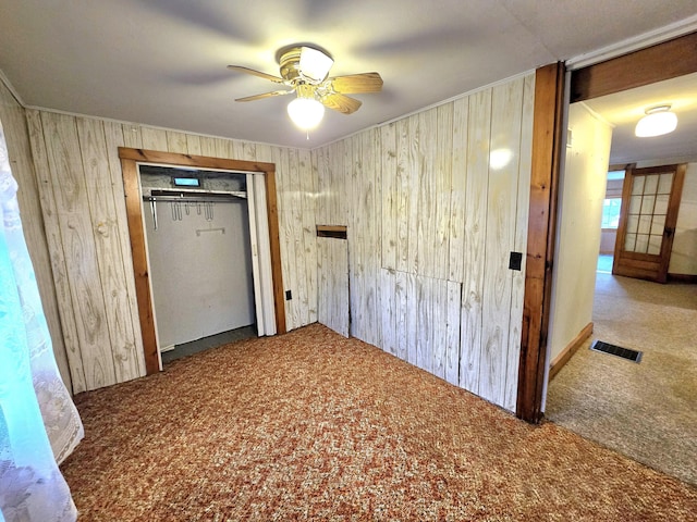 unfurnished bedroom with carpet flooring, ceiling fan, a closet, and wood walls