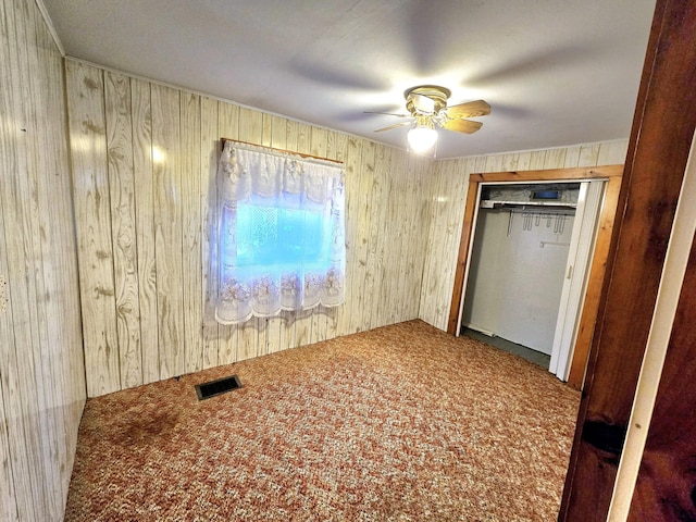 unfurnished bedroom with carpet flooring, ceiling fan, wood walls, and a closet