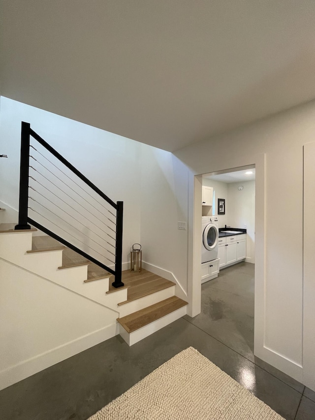 stairs with concrete flooring, washer / dryer, and sink