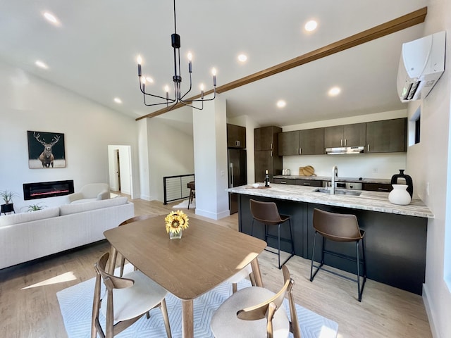 dining space with sink, high vaulted ceiling, an AC wall unit, a chandelier, and light hardwood / wood-style floors