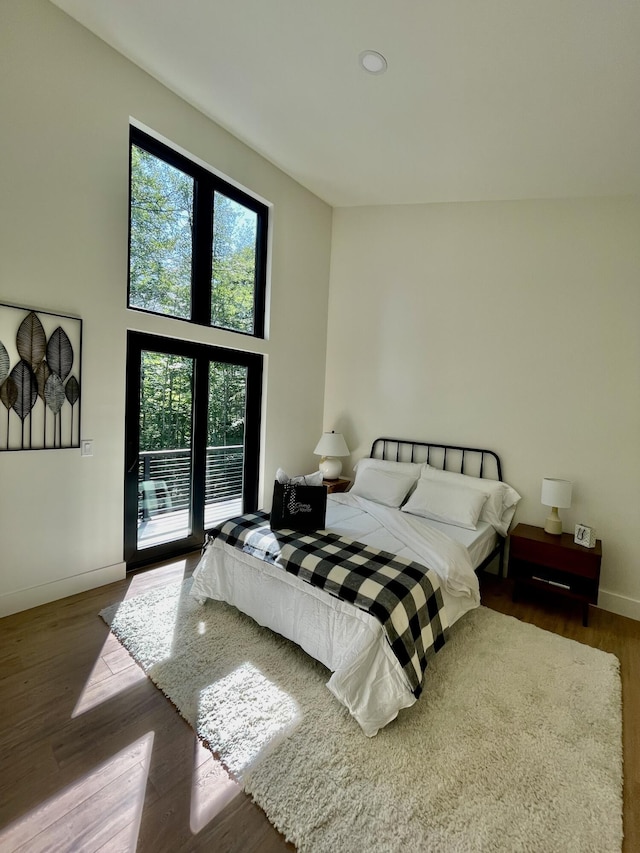 bedroom featuring access to exterior, dark hardwood / wood-style flooring, and a towering ceiling