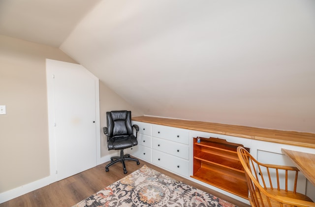 office featuring light hardwood / wood-style floors, lofted ceiling, and built in desk