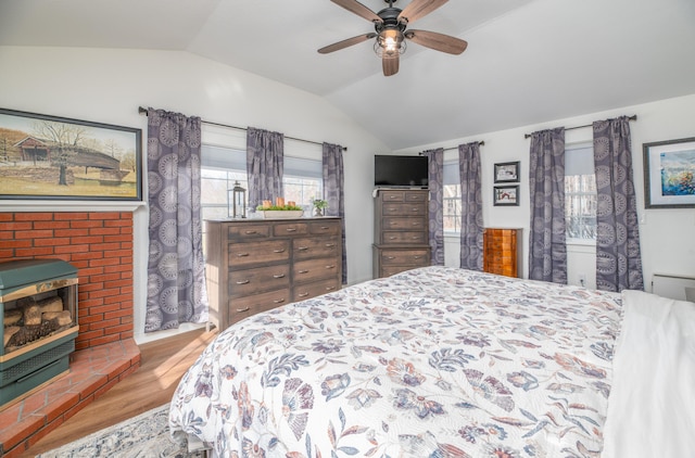 bedroom with ceiling fan, a wood stove, hardwood / wood-style flooring, and vaulted ceiling