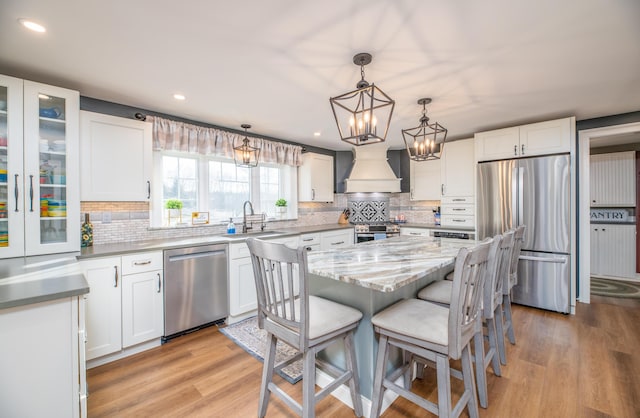 kitchen featuring appliances with stainless steel finishes, a kitchen island, decorative light fixtures, white cabinetry, and premium range hood