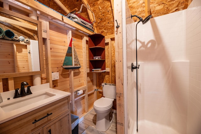 bathroom featuring toilet, vanity, a shower, and wood walls