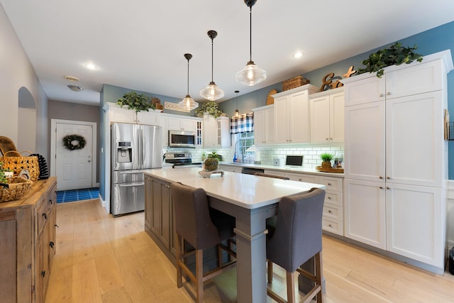 kitchen with a center island, appliances with stainless steel finishes, hanging light fixtures, and white cabinetry