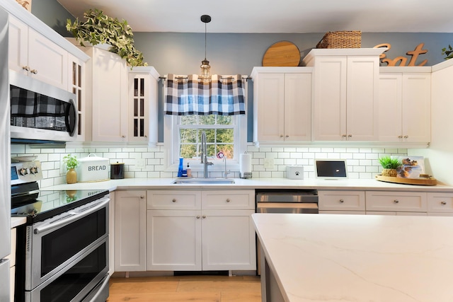 kitchen with stainless steel appliances, light stone countertops, sink, white cabinetry, and decorative light fixtures