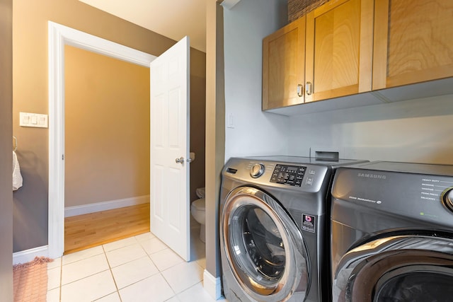 laundry area with washer and dryer, light tile patterned floors, and cabinets