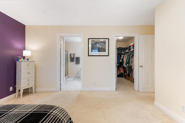 bedroom with ensuite bathroom, a closet, light carpet, and a spacious closet