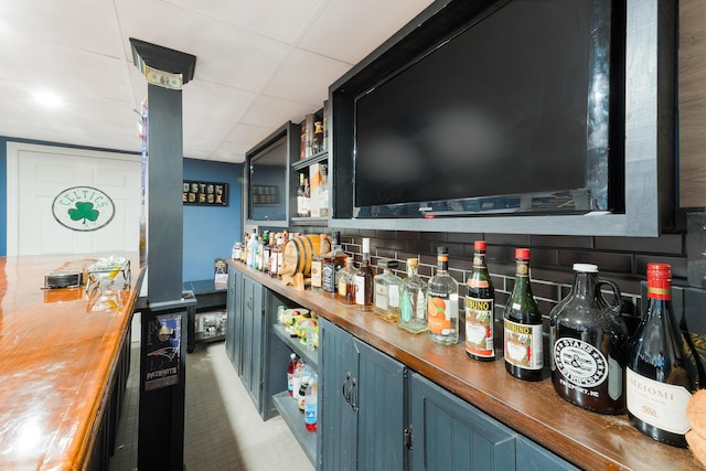 bar featuring blue cabinets, a drop ceiling, backsplash, and wood counters