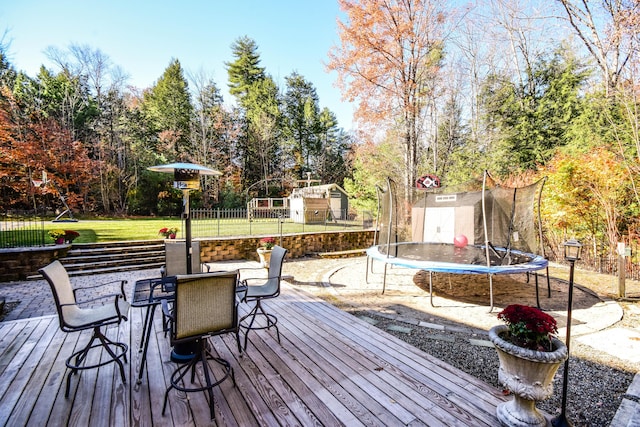 wooden terrace featuring a storage unit, a yard, and a trampoline