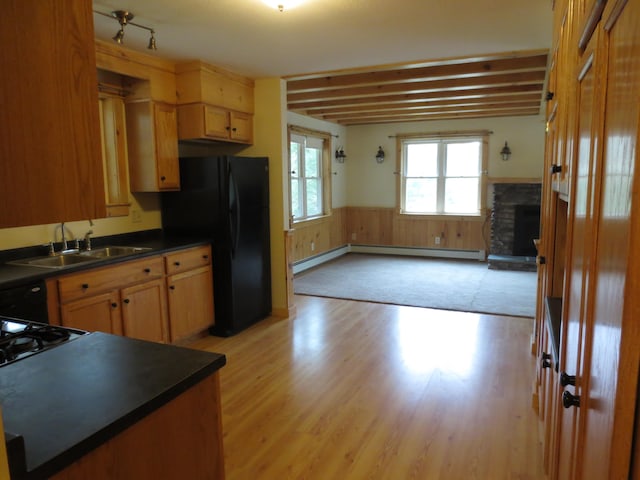 kitchen with a baseboard heating unit, black refrigerator, sink, light wood-type flooring, and beam ceiling