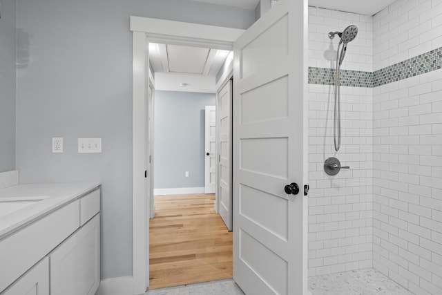 full bath featuring baseboards, wood finished floors, vanity, and a tile shower
