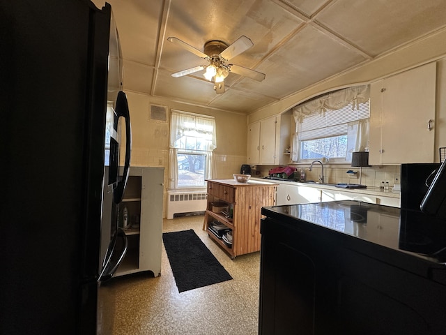 kitchen with white cabinets, black fridge, ceiling fan, tasteful backsplash, and radiator heating unit