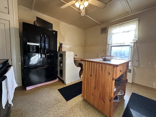 kitchen featuring black fridge with ice dispenser, stove, ceiling fan, and radiator