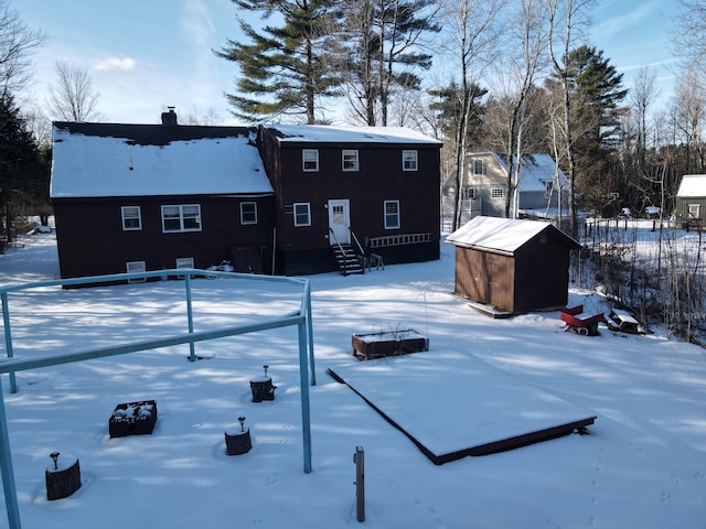 snow covered rear of property featuring a storage shed