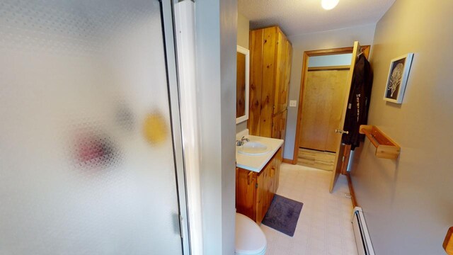 bathroom featuring a baseboard heating unit, toilet, a shower with shower door, and vanity