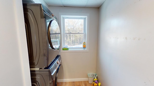 laundry area featuring stacked washer and clothes dryer and light hardwood / wood-style flooring