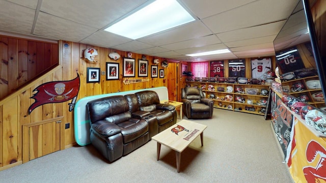 living room with a drop ceiling, carpet, and wooden walls