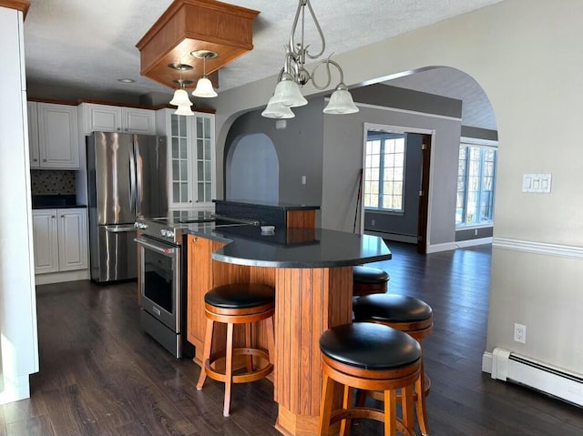 kitchen featuring white cabinets, stainless steel appliances, a kitchen bar, and baseboard heating