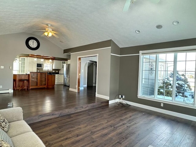 unfurnished living room featuring a textured ceiling, a baseboard heating unit, dark hardwood / wood-style floors, vaulted ceiling, and ceiling fan