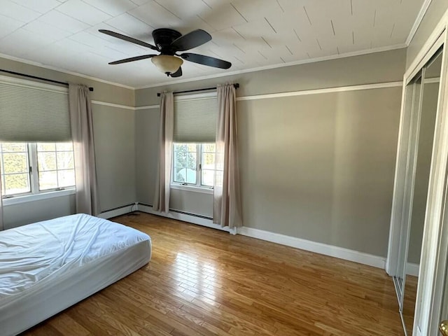 unfurnished bedroom with ceiling fan, crown molding, baseboard heating, and wood-type flooring